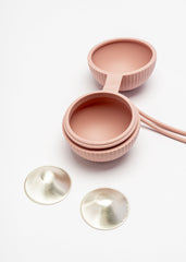 Silverette Happy Nipples pink silicone holder, open, with two Silverette silver nursing cups beside it